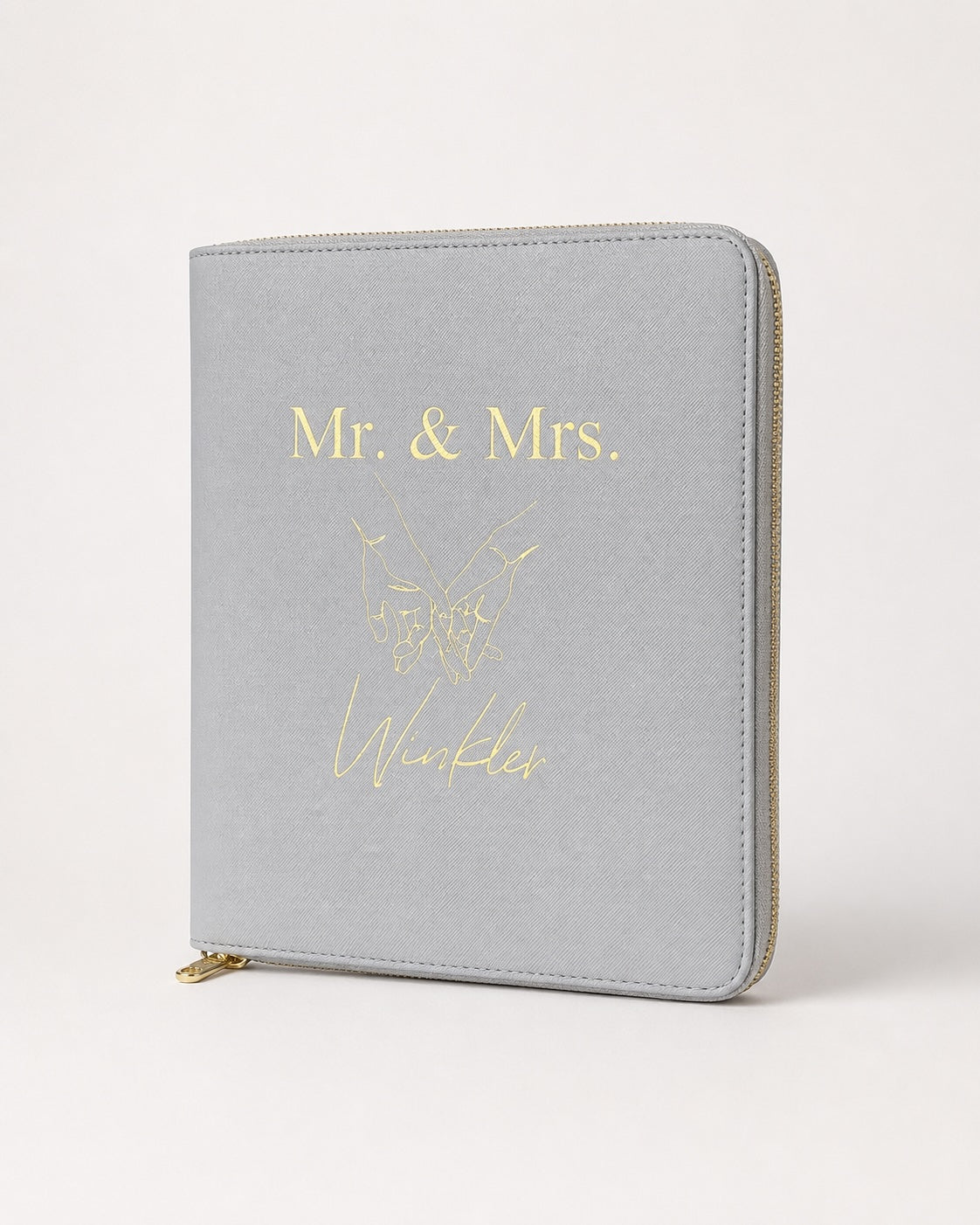 Personalisierter hellgrauer Reiseorganizer mit goldenem „Mr. & Mrs. Winkler“-Aufdruck und Handmotiv auf neutralem Hintergrund.