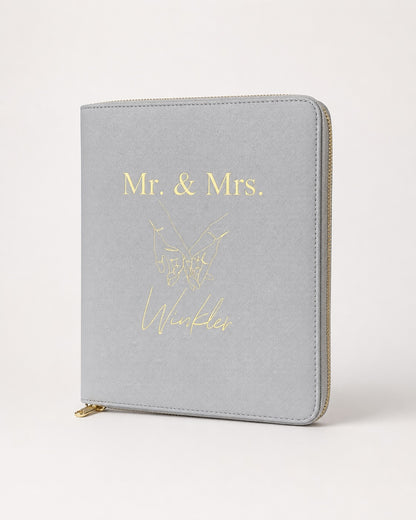 Personalisierter hellgrauer Reiseorganizer mit goldenem „Mr. & Mrs. Winkler“-Aufdruck und Handmotiv auf neutralem Hintergrund.