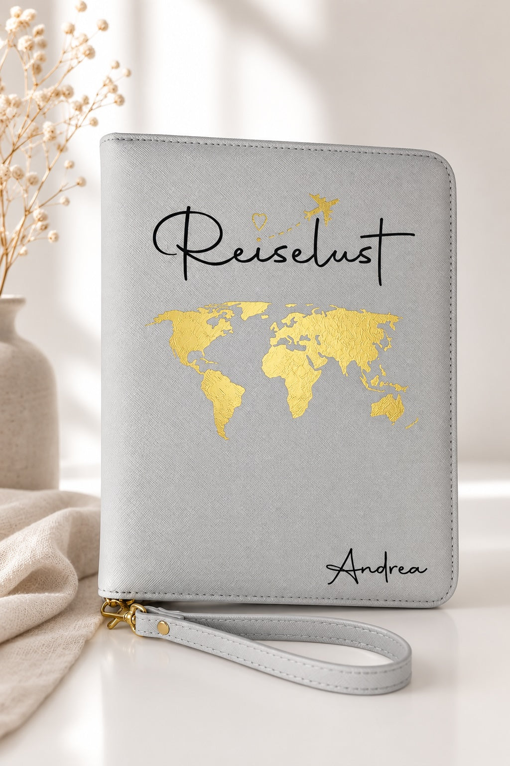 Grauer personalisierter Reiseorganizer mit goldenem Weltkarten-Motiv, schwarzem Schriftzug „Reiselust“ und dem Namen Andrea in einer hellen, ästhetischen Produktkulisse.