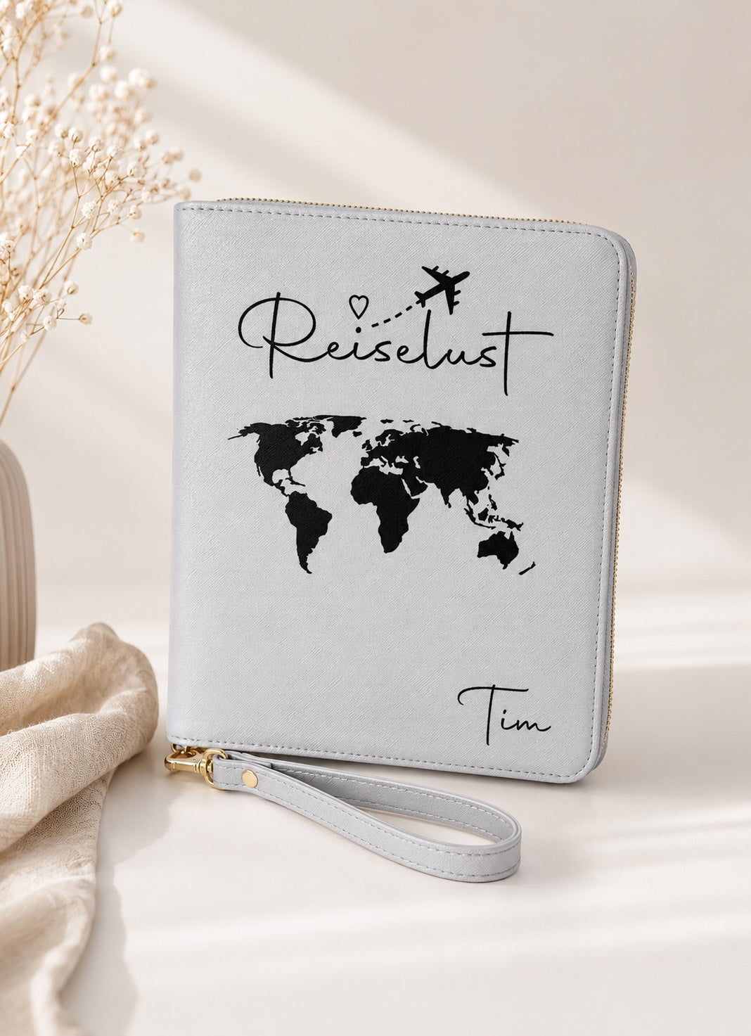 Grauer personalisierter Reiseorganizer mit schwarzem Schriftzug „Reiselust“, schwarzer Weltkarte und dem Namen Tim vor hellem, ästhetischem Hintergrund.