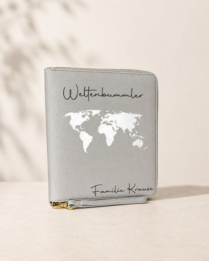 Grauer personalisierter Reiseorganizer mit weißer Weltkarte, schwarzem Schriftzug „Weltenbummler“ und der Personalisierung „Familie Krause“ vor hellem neutralem Hintergrund.
