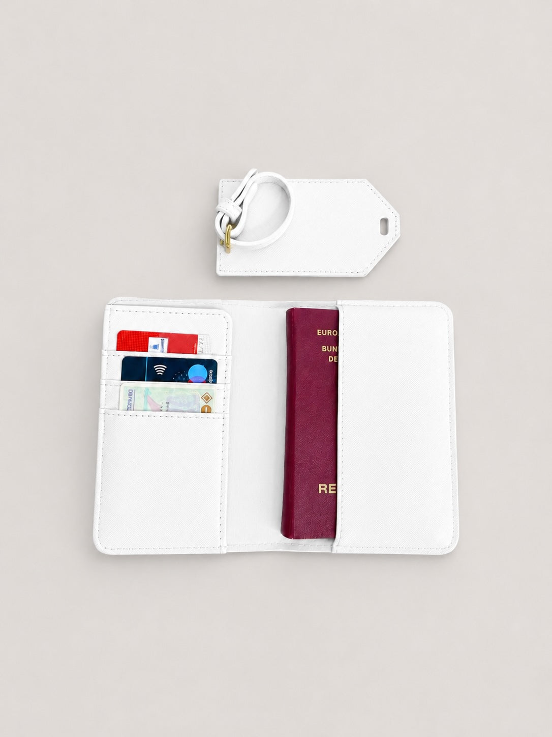 Minimalistisches Produktfoto einer weißen Reisepasshülle mit Kofferanhänger und Dokumentenmappe auf hellem, neutralem Hintergrund, mit sichtbarer Karte und Kartenfächern im Inneren.