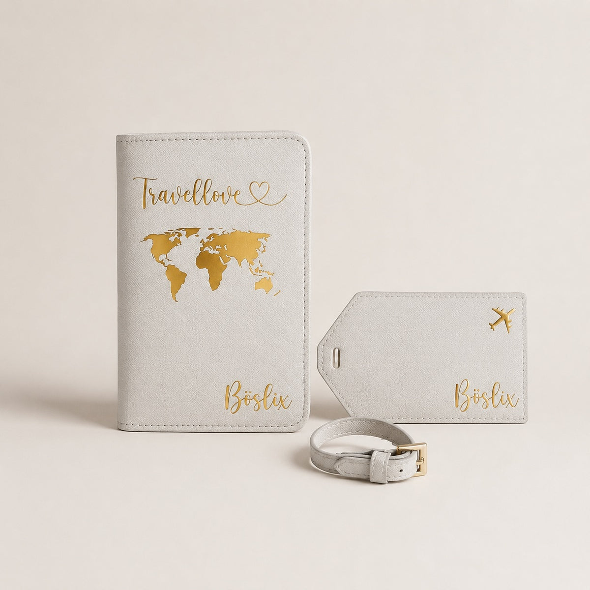 Ästhetisches Produktbild eines personalisierten Reiseaccessoire-Sets in Weiß mit goldfarbenem, leicht schimmerndem Aufdruck. Zu sehen sind eine Reisepasshülle mit Weltkartenmotiv, ein passender Kofferanhänger mit kleinem Flugzeug und eine Schlaufe auf neutralem Hintergrund.
