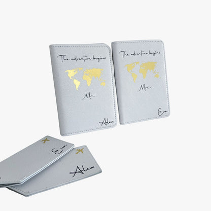 Hellgraues  Set aus zwei personalisierten Reisepasshüllen mit goldener Weltkarte und der Aufschrift „The adventure begins“, inklusive Kofferanhängern – ideales Hochzeits- oder Flitterwochen-Geschenk.
