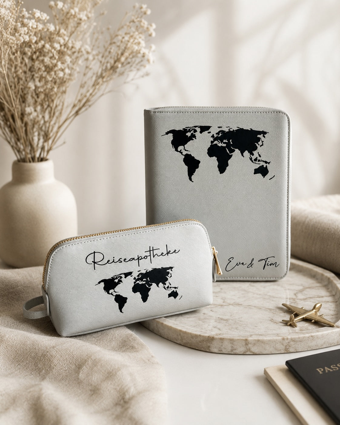 Ästhetisches Produktbild eines hellgrauen Reisesets mit Reiseapotheke und Reise-Organizer mit Weltkartenmotiv, dekoriert mit Trockenblumen, Leinentuch und Reiseaccessoires.