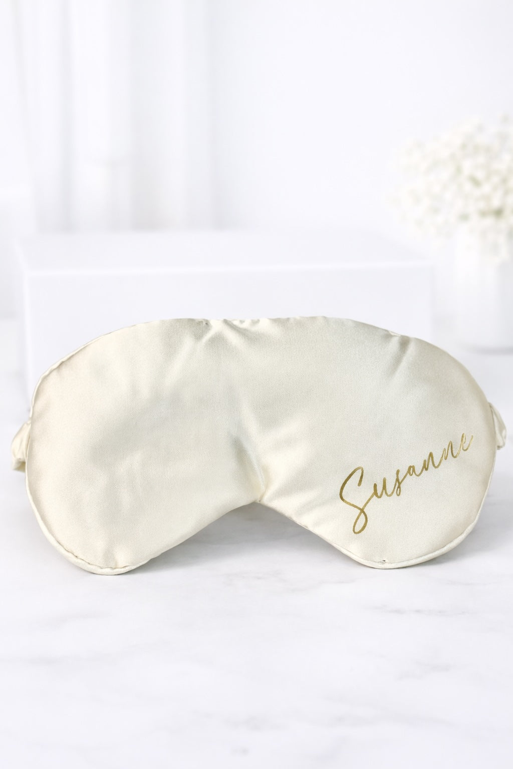 Personalisierte Schlafmaske aus Satin in Creme mit goldener Aufschrift „Susanne“ auf hellem Hintergrund