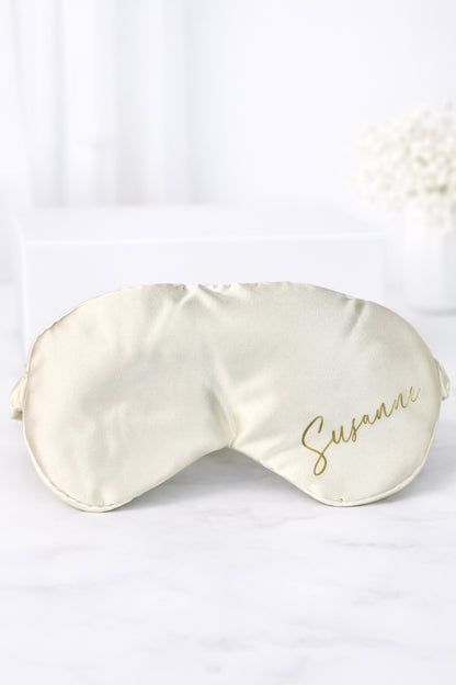 Personalisierte Schlafmaske aus Satin in Creme mit goldener Aufschrift „Susanne“ auf hellem Hintergrund