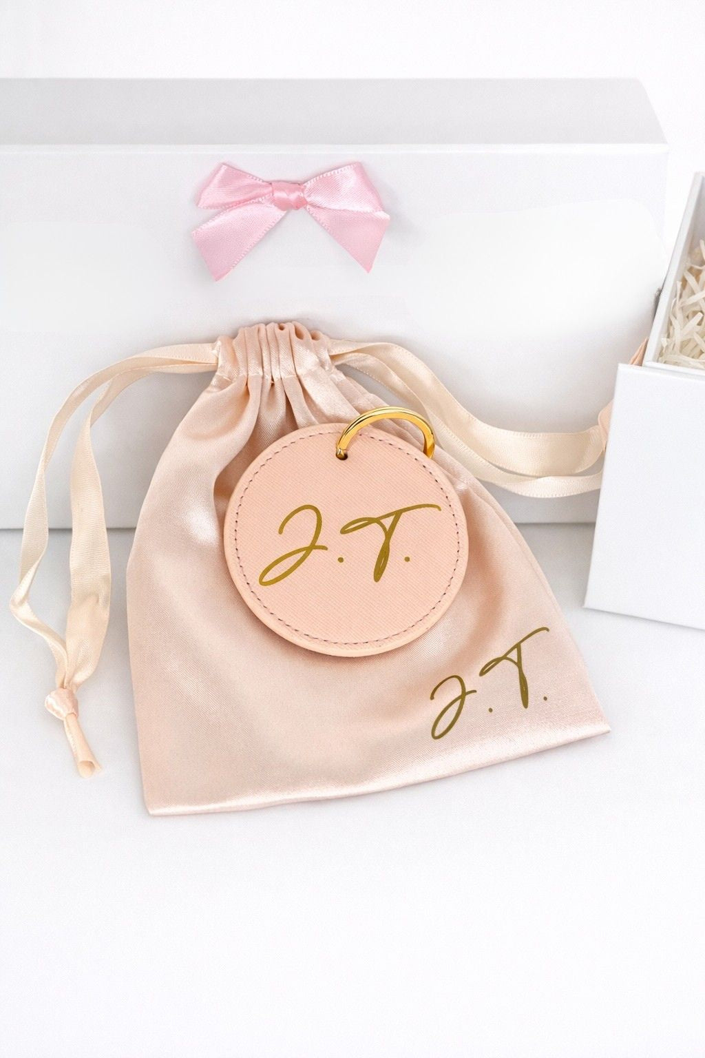 Personalisierter rosa Schlüsselanhänger im Satinbeutel vor weißer Geschenkbox mit pinker Schleife