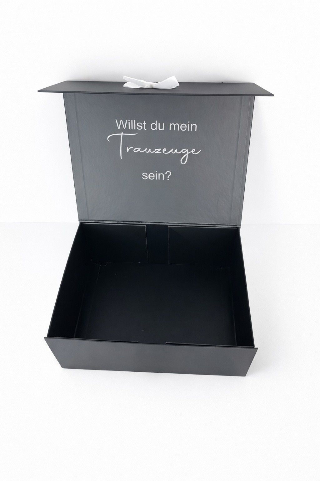 Schwarze Geschenkbox mit Aufschrift ‚Willst du mein Trauzeuge sein?‘, geöffnet und bereit zum Befüllen als persönliche Überraschung zur Hochzeit