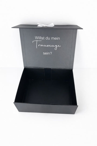 Schwarze Geschenkbox mit Aufschrift ‚Willst du mein Trauzeuge sein?‘, geöffnet und bereit zum Befüllen als persönliche Überraschung zur Hochzeit