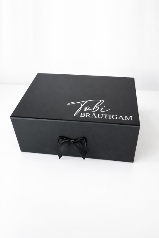 Personalisierte schwarze Geschenkbox für den Bräutigam mit Aufdruck „Tobi Bräutigam“, Magnetverschluss und schwarzer Schleife auf hellem neutralen Hintergrund.
