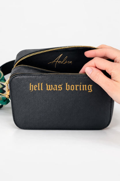 Schwarze Damen Umhängetasche mit goldener Aufschrift „hell was boring“ und personalisiertem Namen „Andrea“ im Innenfach auf hellem neutralem Hintergrund.