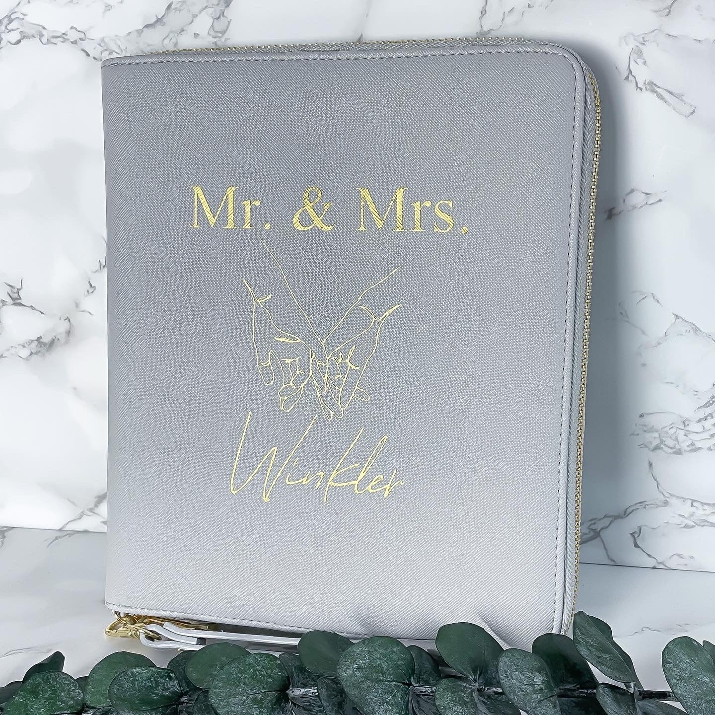 Personalisierter Dokumentenorganizer in Grau mit goldenem Aufdruck „Mrs. & Mrs.“ zur Aufbewahrung von Reiseunterlagen.