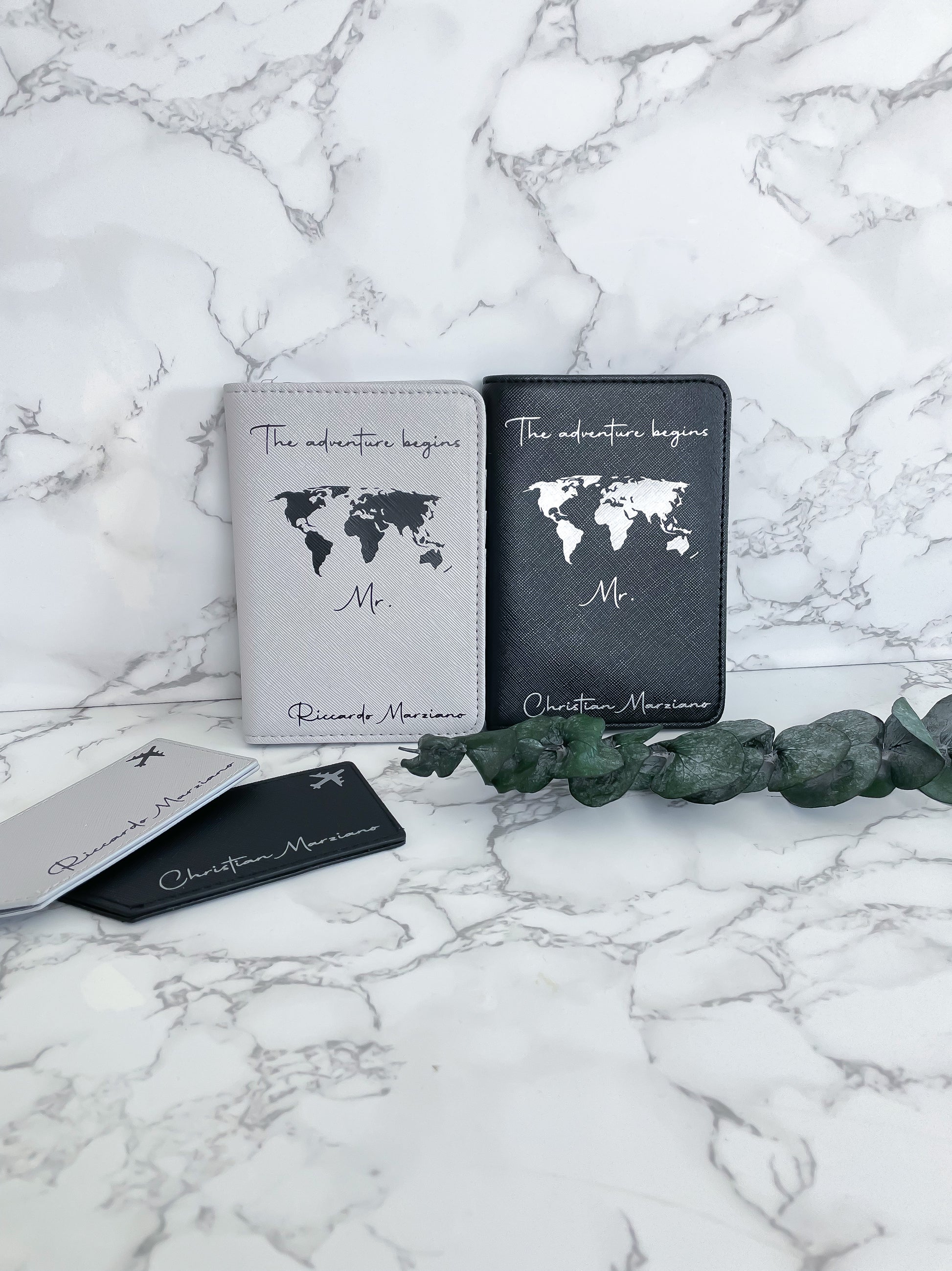 Personalisierte Reisepasshüllen „The adventure begins“ in Schwarz und Weiß mit Weltkarte und Kofferanhängern – ideales Hochzeits- oder Reisegeschenk für Paare.