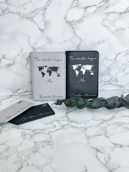 Personalisierte Reisepasshüllen „The adventure begins“ in Schwarz und Weiß mit Weltkarte und Kofferanhängern – ideales Hochzeits- oder Reisegeschenk für Paare.