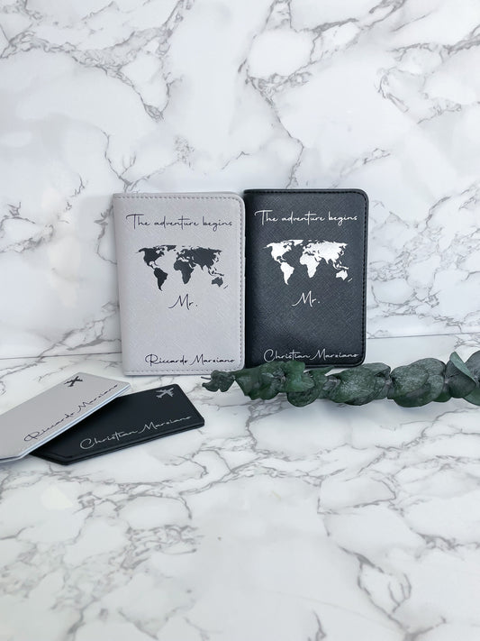 Personalisierte Reisepasshüllen „The adventure begins“ in Schwarz und Weiß mit Weltkarte und Kofferanhängern – ideales Hochzeits- oder Reisegeschenk für Paare.